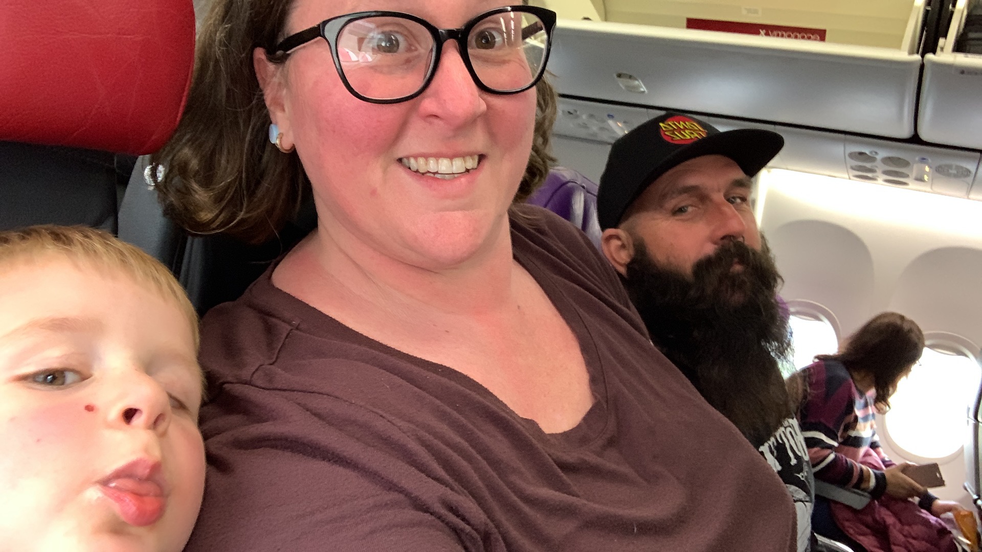 A child, woman and man sitting on a plane smile for a selfie