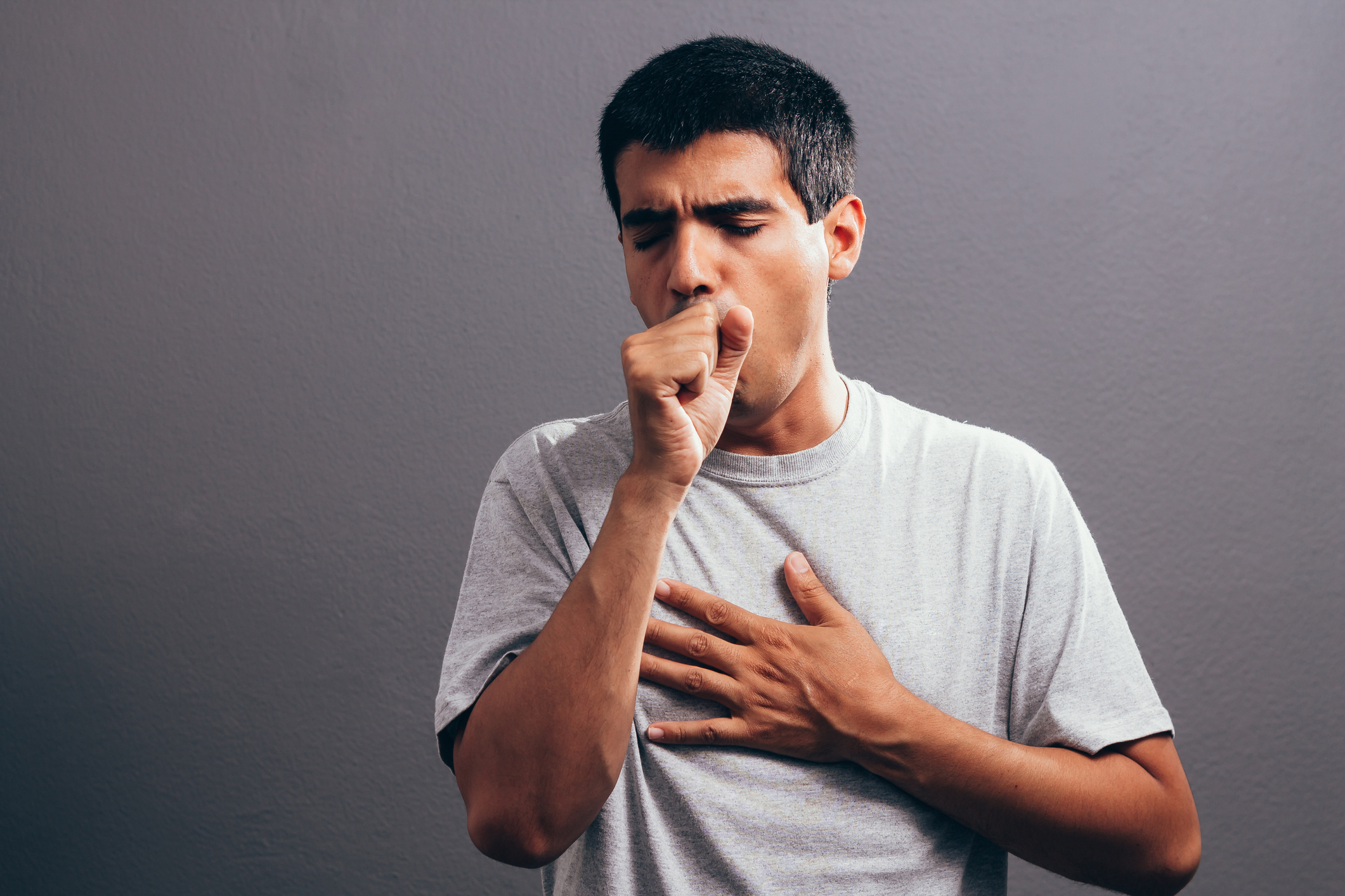  A young man is covering his mouth and nose with his arm while coughing.