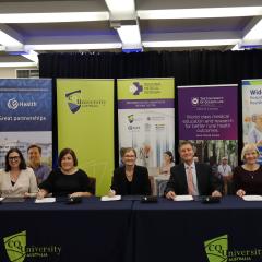 Five adults sitting at desk with black tablecloth, smiling looking at camera
