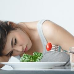 Unhappy woman looking at tomato on fork