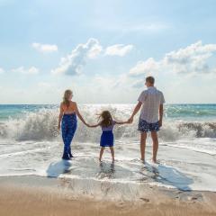 family of three standing on a beach facing the waves
