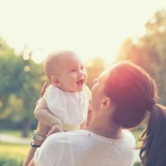 mother lifting baby up outside in a park