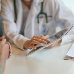 A doctor's hand hovering over a clipboard opposite a patient's hand 